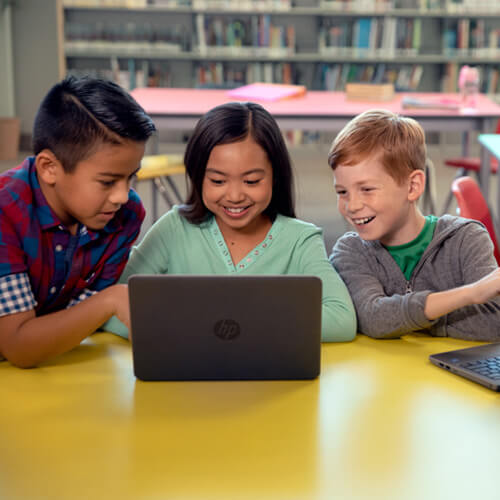 Students sharing a laptop in the school library, smiling