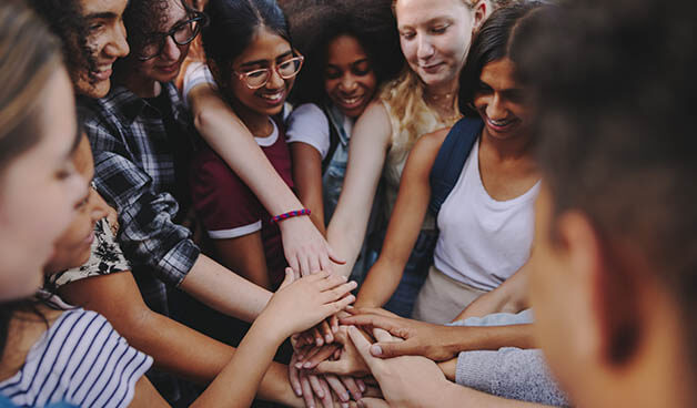 Group of happy teenagers putting their hands together in a huddle